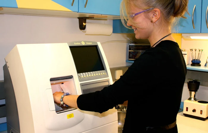 Eine Frau arbeitet am Computergesteuerter Automat zur Glasrundung bei Augenoptik Schmetterer in Prien