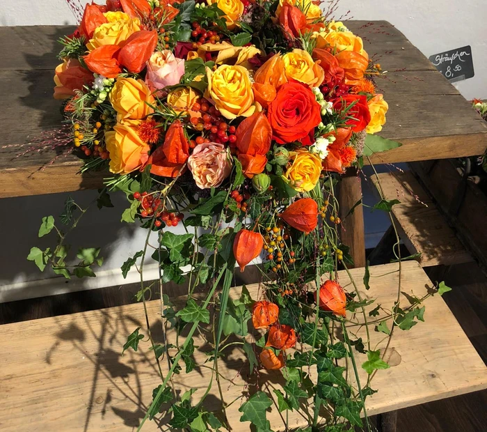Trauergesteck mit gelben und orangen Rosen mit Efeu