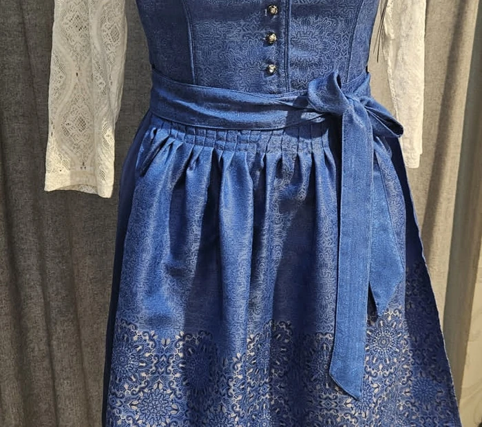 Präsentiert wird ein blaues Dirndl mit weißer Bluse, erhältlich in der Chiceria Prien, solange Vorrat reicht