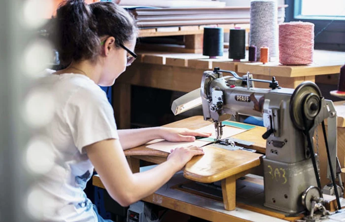 In der Buchbinderei Bindewerk Prien sitzt eine Frau vor einer Nähmaschine und näht Bucheinbände