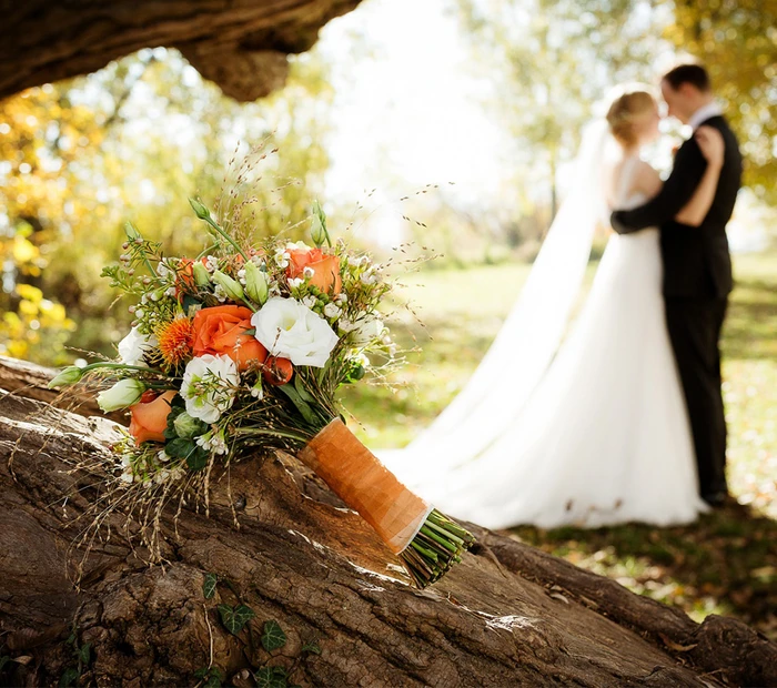 Im Vordergrund ein Brautstrauß in den Farben orange-weiß-grün und im Hintergrund das Brautpaar.