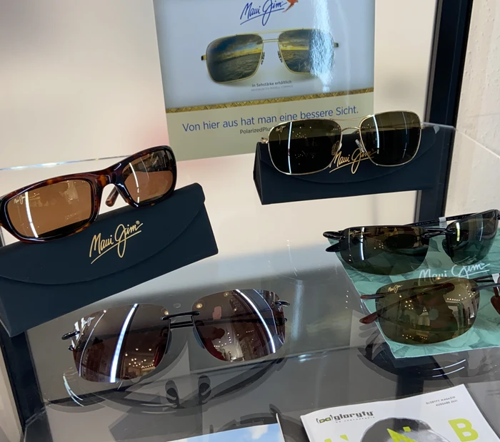 5 verschiedene Sonnebrillen von Maui Jim mit Etui werden auf eine Glastisch prästentiert.
