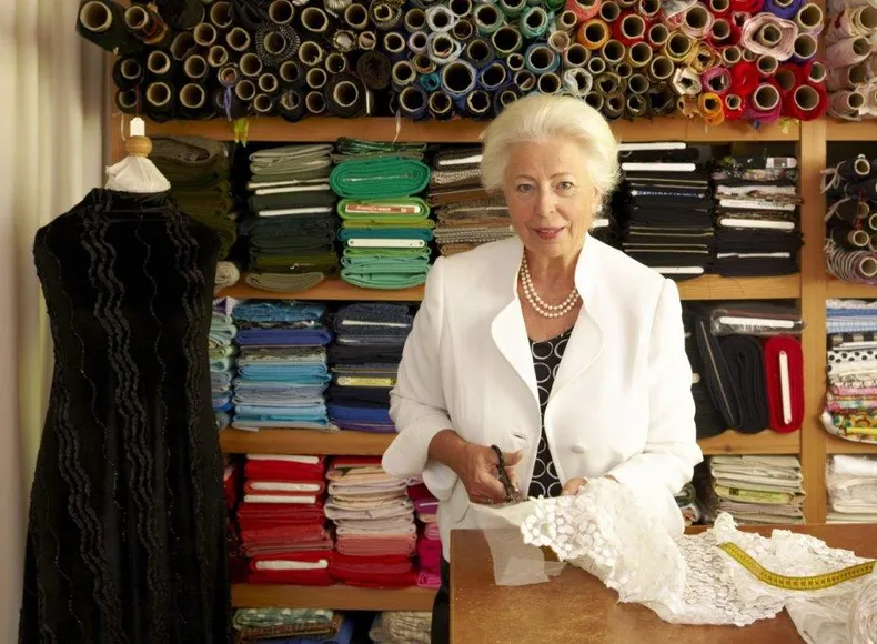 Frau Gerdi Westermeyr in ihren Atelier beim Zuschnitt, im Hintergrund sind verschiedene Stoffballen zu sehen.