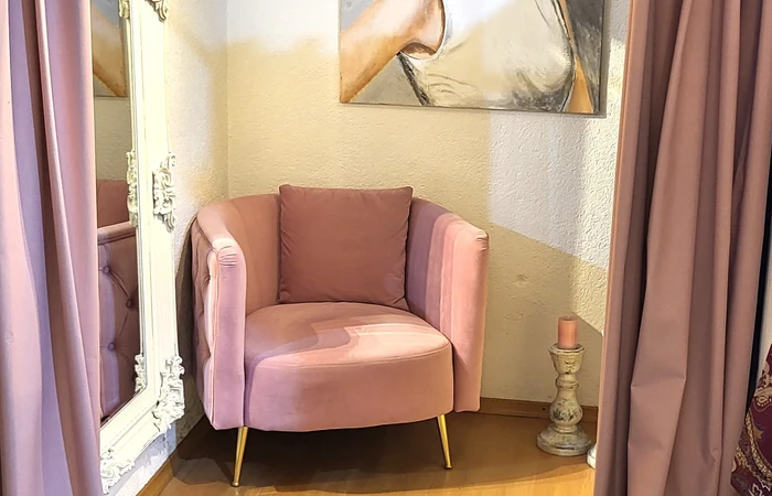 Umkleide in der Boutique Kunstwerkstatt gemütlich mit rosa Samtvorhängen und Samt Sessel mit Goldelementen , Bild einer feinen Dame im Hintergrund