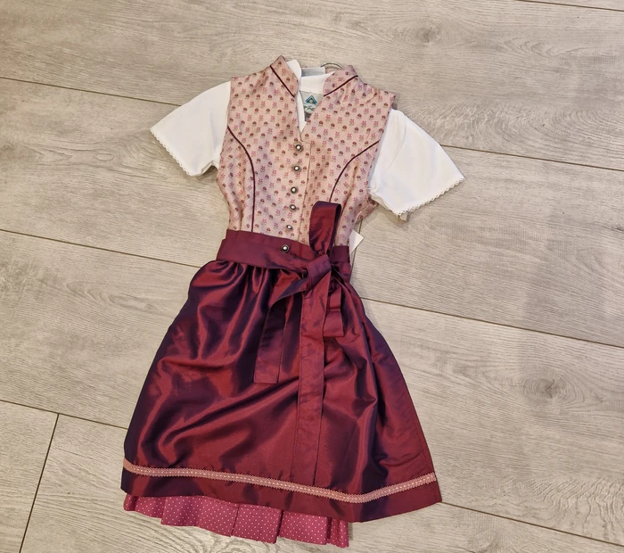 Präsentiert wird ein rosa-bordeauxfarbenes Kinderdirndl mit Bluse, erhältlich in der Chiceria solange der Vorrat reicht