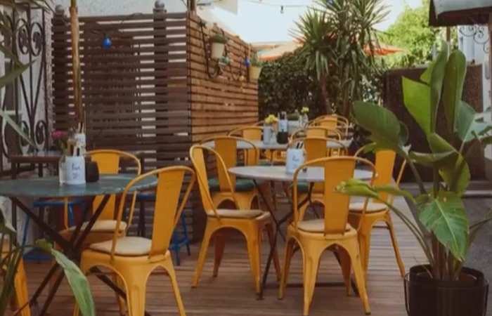 die Pura Terrasse in Prien ist gemütlich mit orangenen Tolix Stühlen, viel Holz und großen Palmen